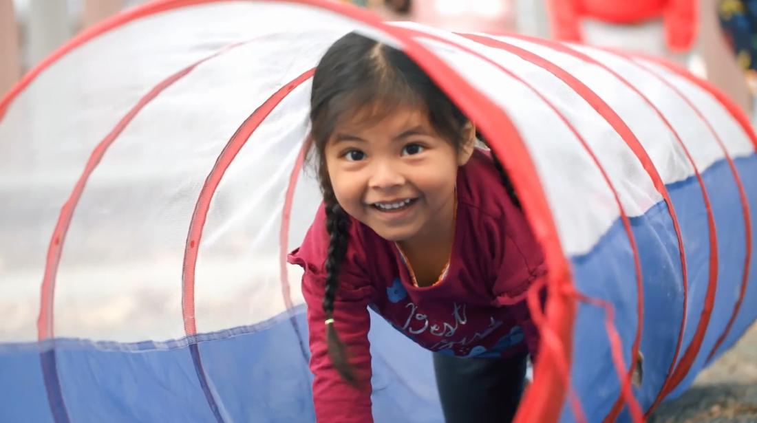 Small child smiling and crawling through toy tunnel