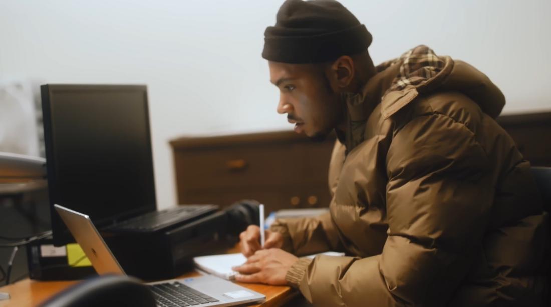 Student taking notes while looking at laptop